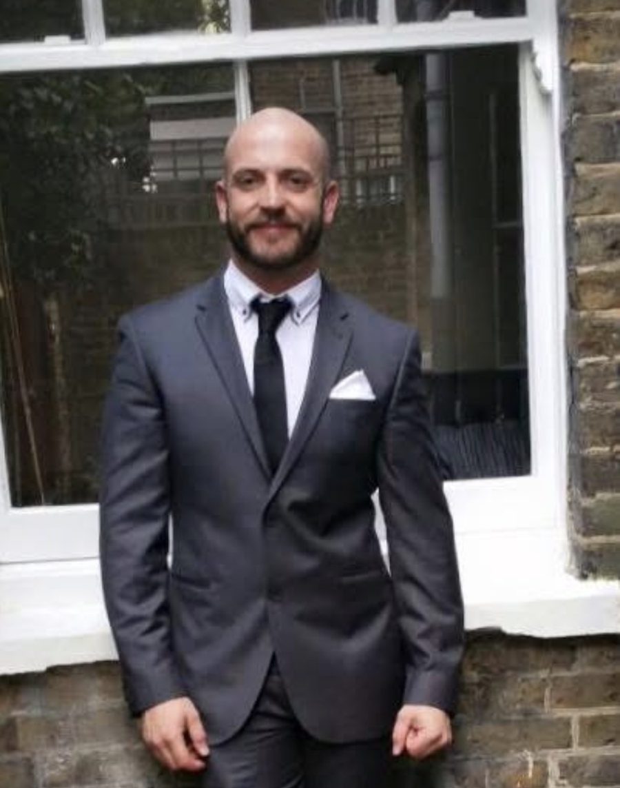William, founder of Wise Journey Support, in a suit outside a brick building in London